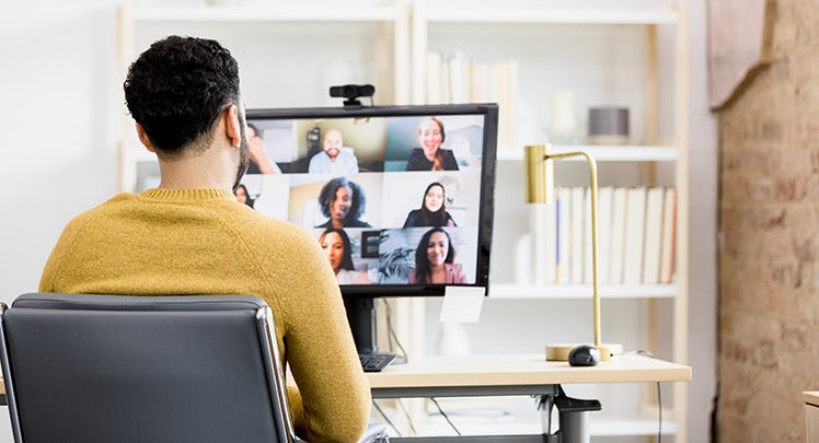 A man sitting in front of a computer with a group of people on a video call.