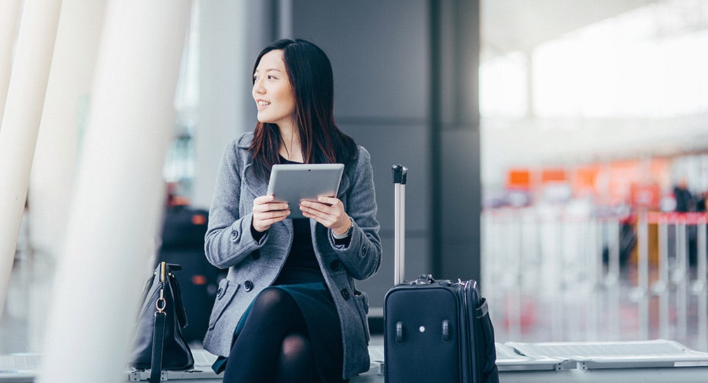 A woman sitting in an airport holding a tablet.