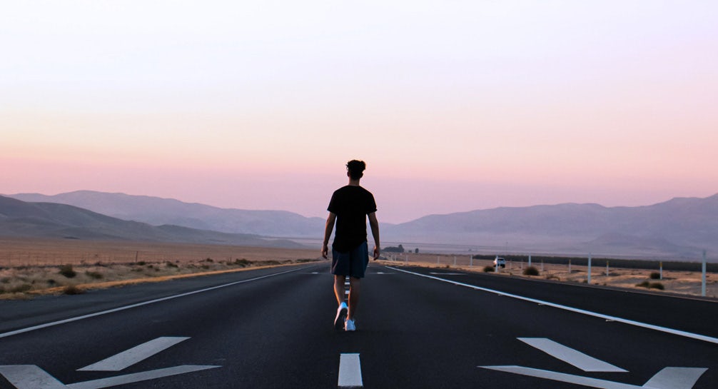 A silhouette of a man walking down an empty road at sunset.